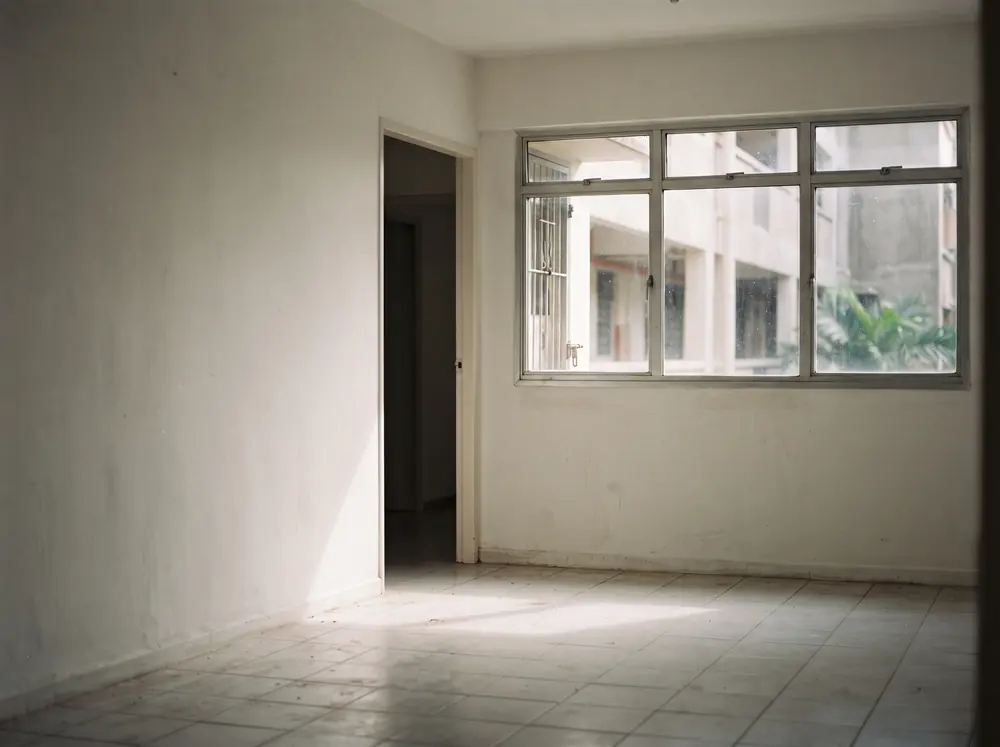 An empty apartment room with bare walls and a single shaft of window light
