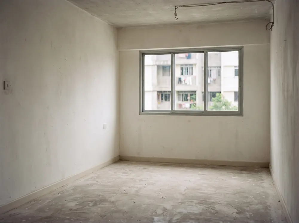 An empty apartment room with bare walls and screed