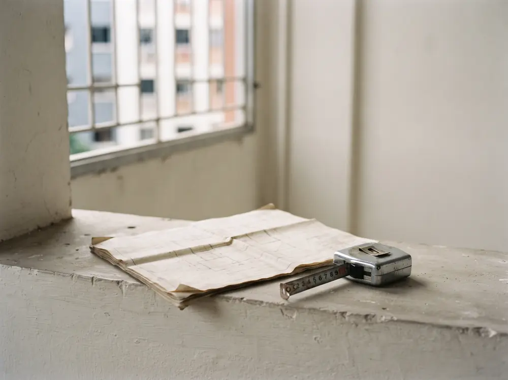 A folded flat plan and a steel measuring tape on a bare windowsill